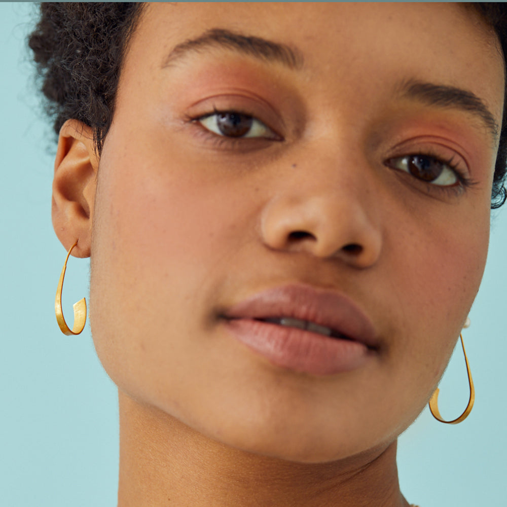 Close-up of a woman wearing gold threader hoop earrings against a light blue background