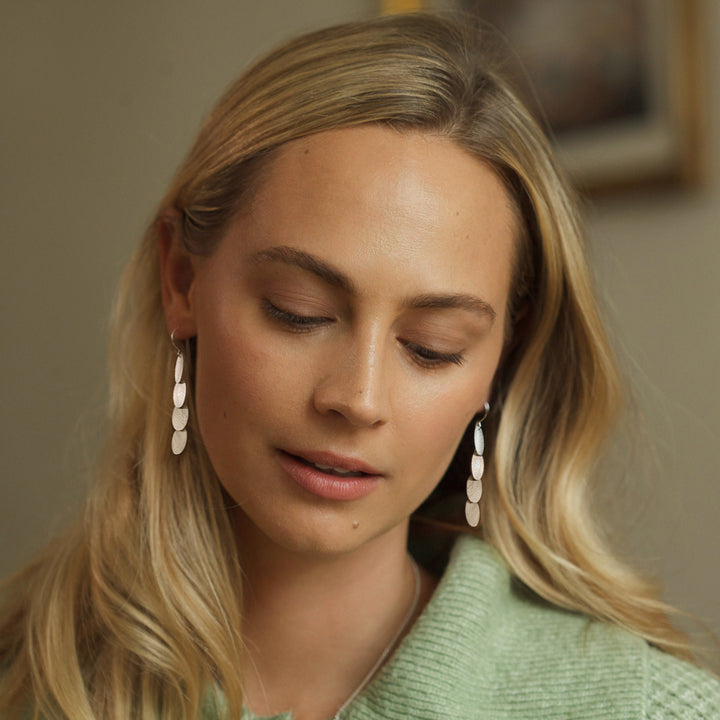 Woman wearing silver dangle earrings with a green sweater