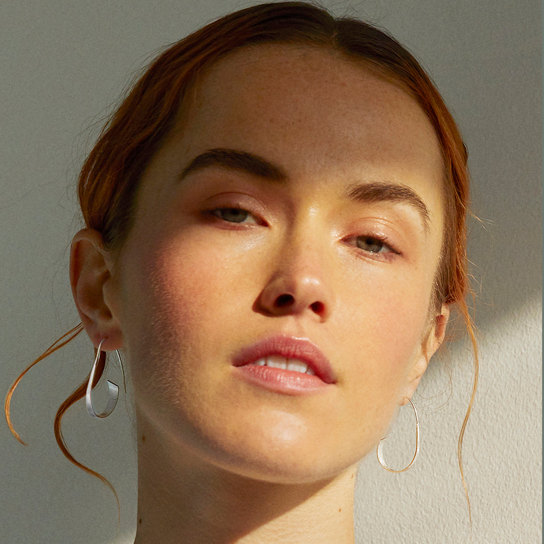 Close-up of a model wearing silver threader hoop earrings against a gray background