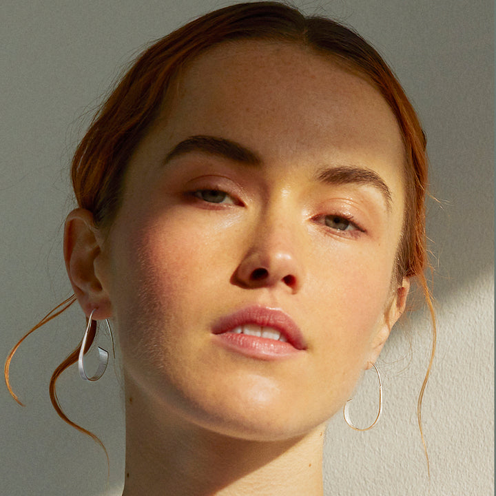 Close-up of a model wearing silver threader hoop earrings against a gray background