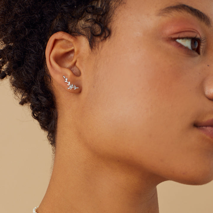 Close-up of a person wearing a silver leaf-shaped earring on a beige background