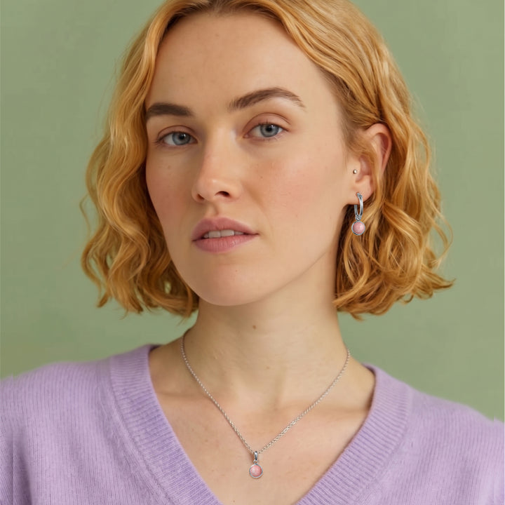 Woman wearing pink opal gemstone huggie hoop earrings and matching pendant necklace in sterling silver 