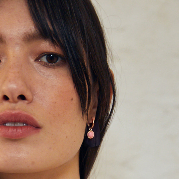 Close-up of woman wearing pink opal huggie hoop earrings in 18ct gold vermeil with a snap post closing