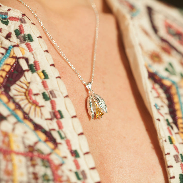 Close-up of a silver floral pod necklace with gold details