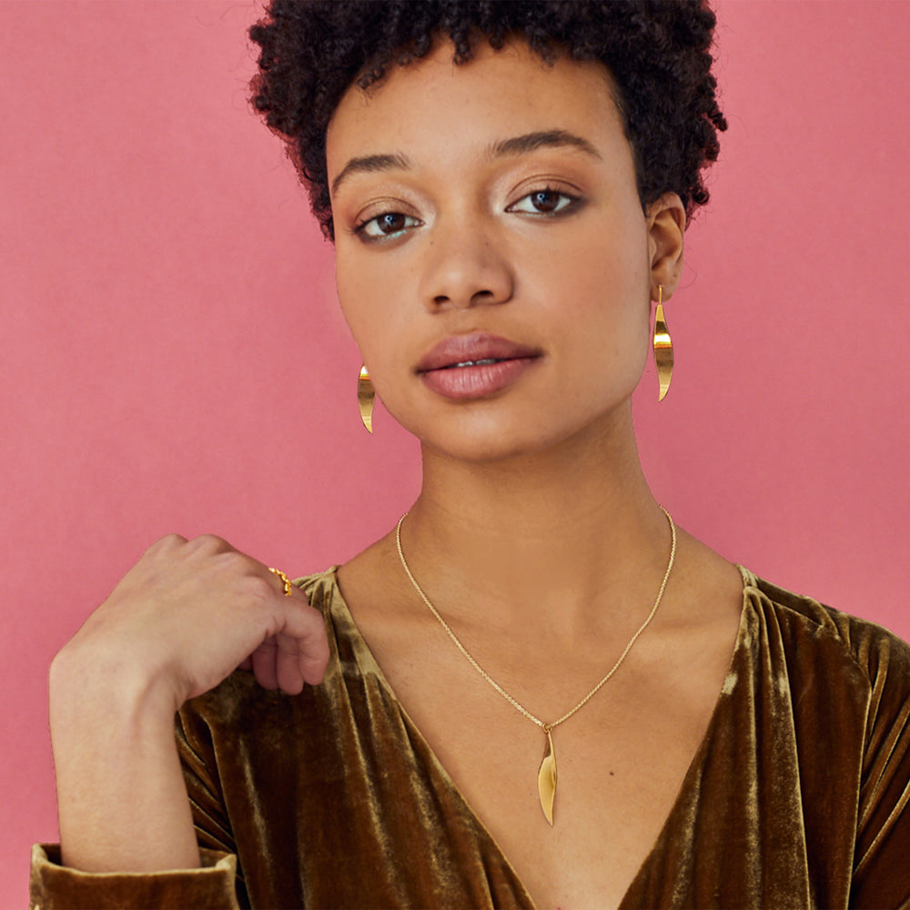 Woman wearing shiny gold jewellery against a pink background