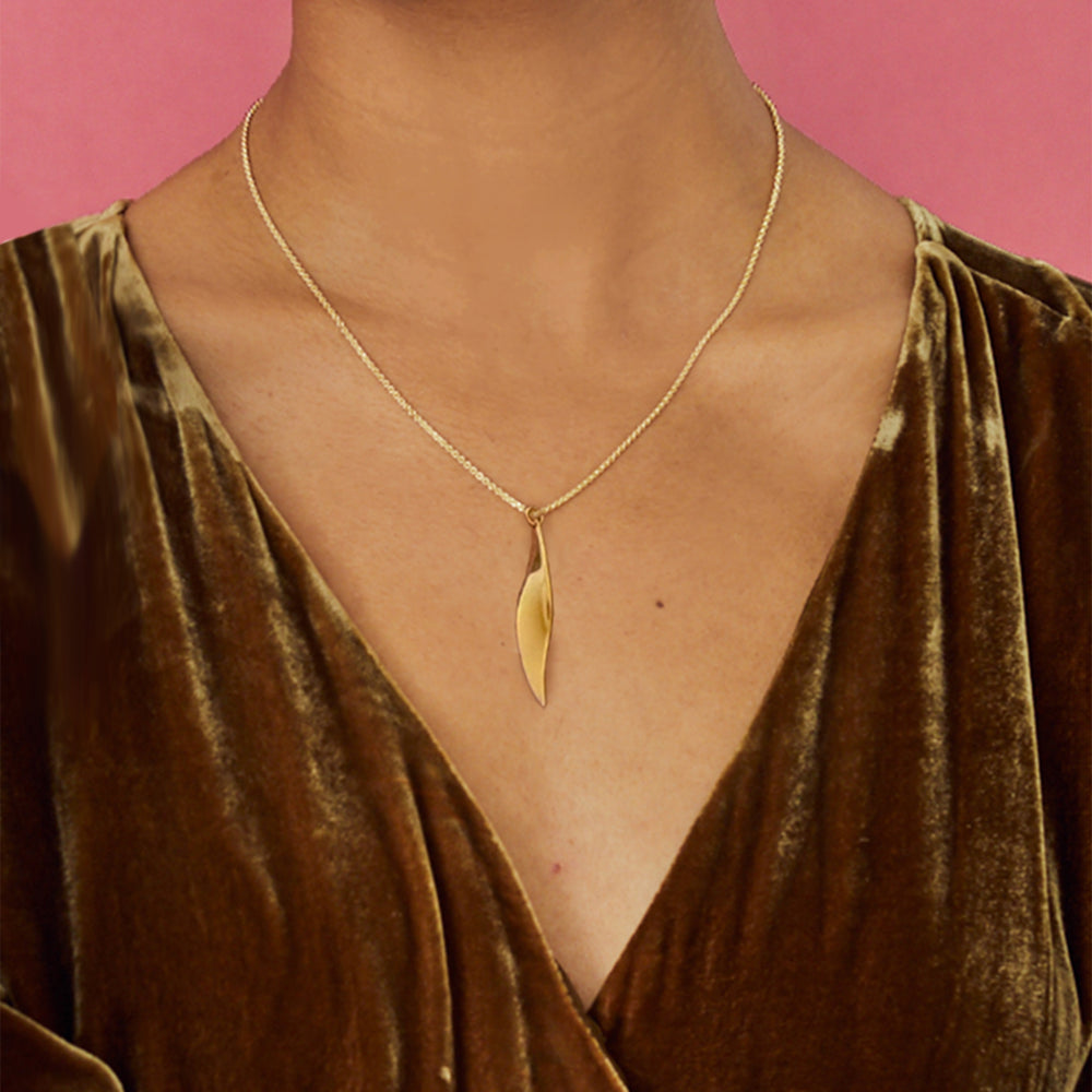Close-up of woman wearing a polished gold vermeil curved pendant necklace on a pink background