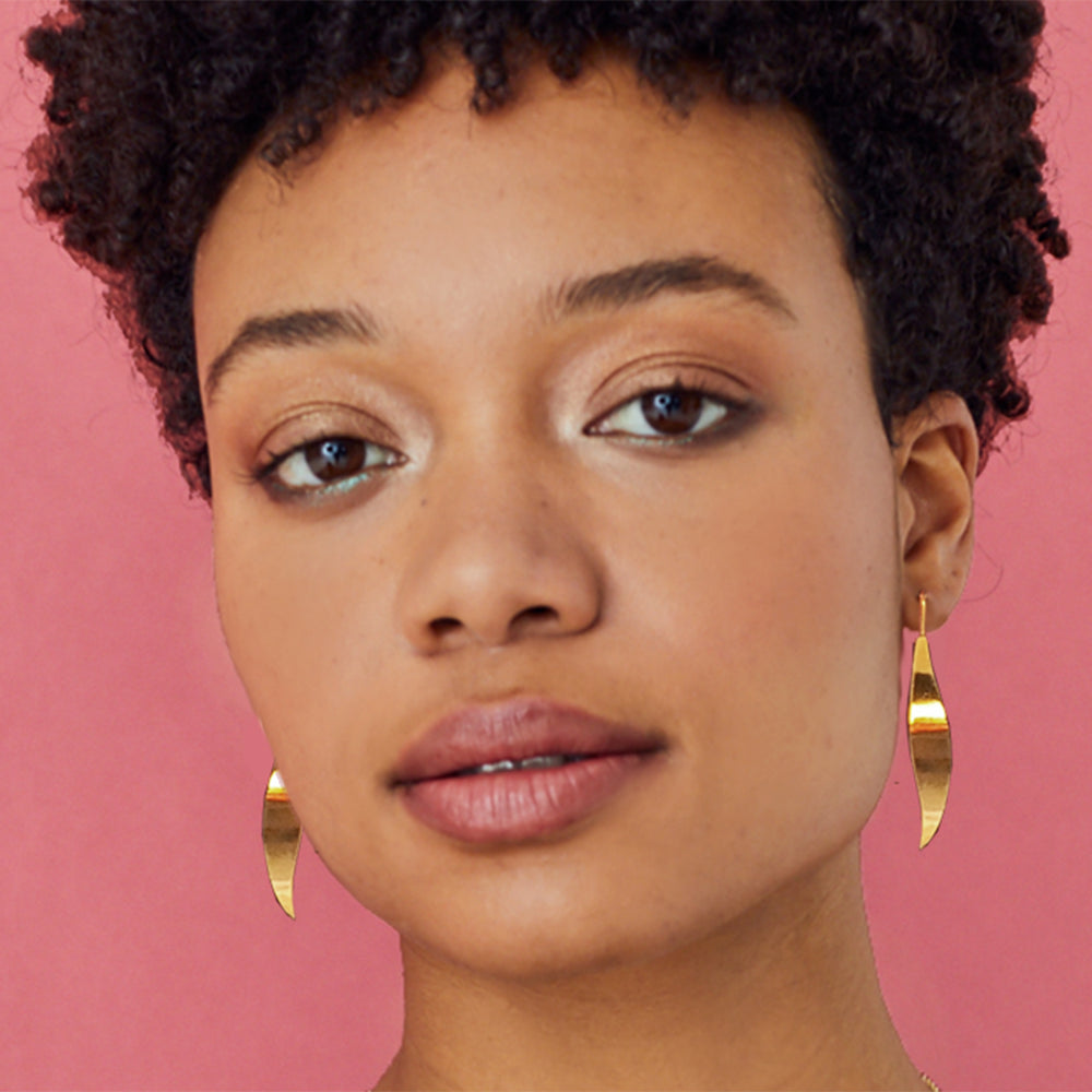 Close-up of a woman wearing gold earrings against a pink background