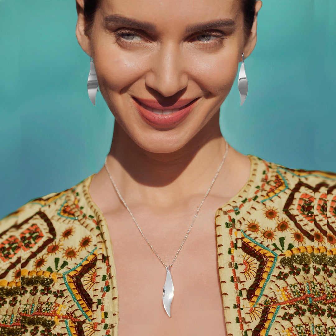 Woman wearing polished silver earrings and necklace on teal background