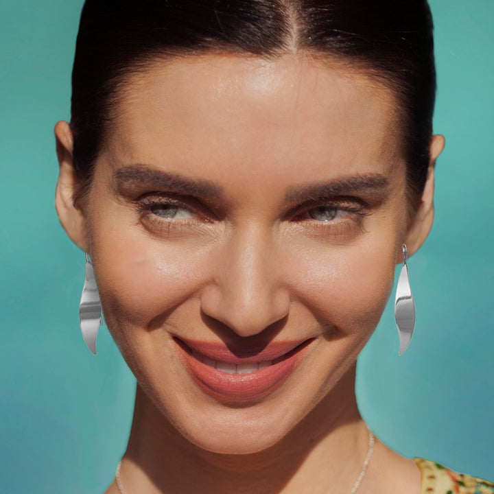 Close-up of a woman with polished silver earrings against a teal background