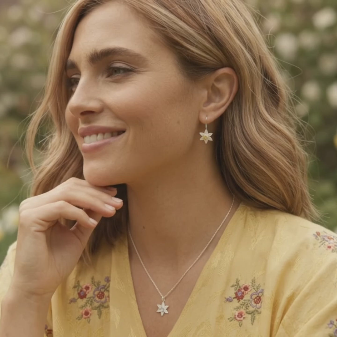 Woman wearing silver daffodil drop earrings and matching necklace in a garden