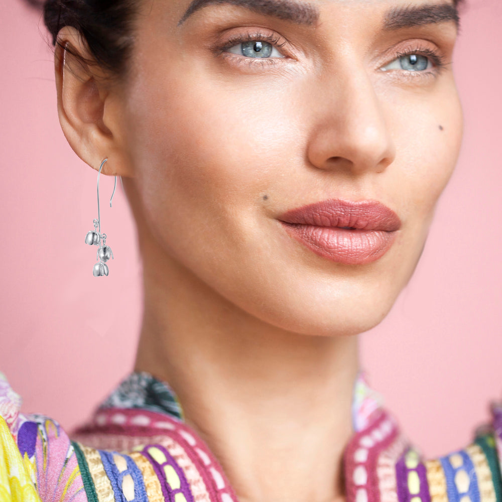 Close-up of a woman wearing silver flower earrings with a pink background