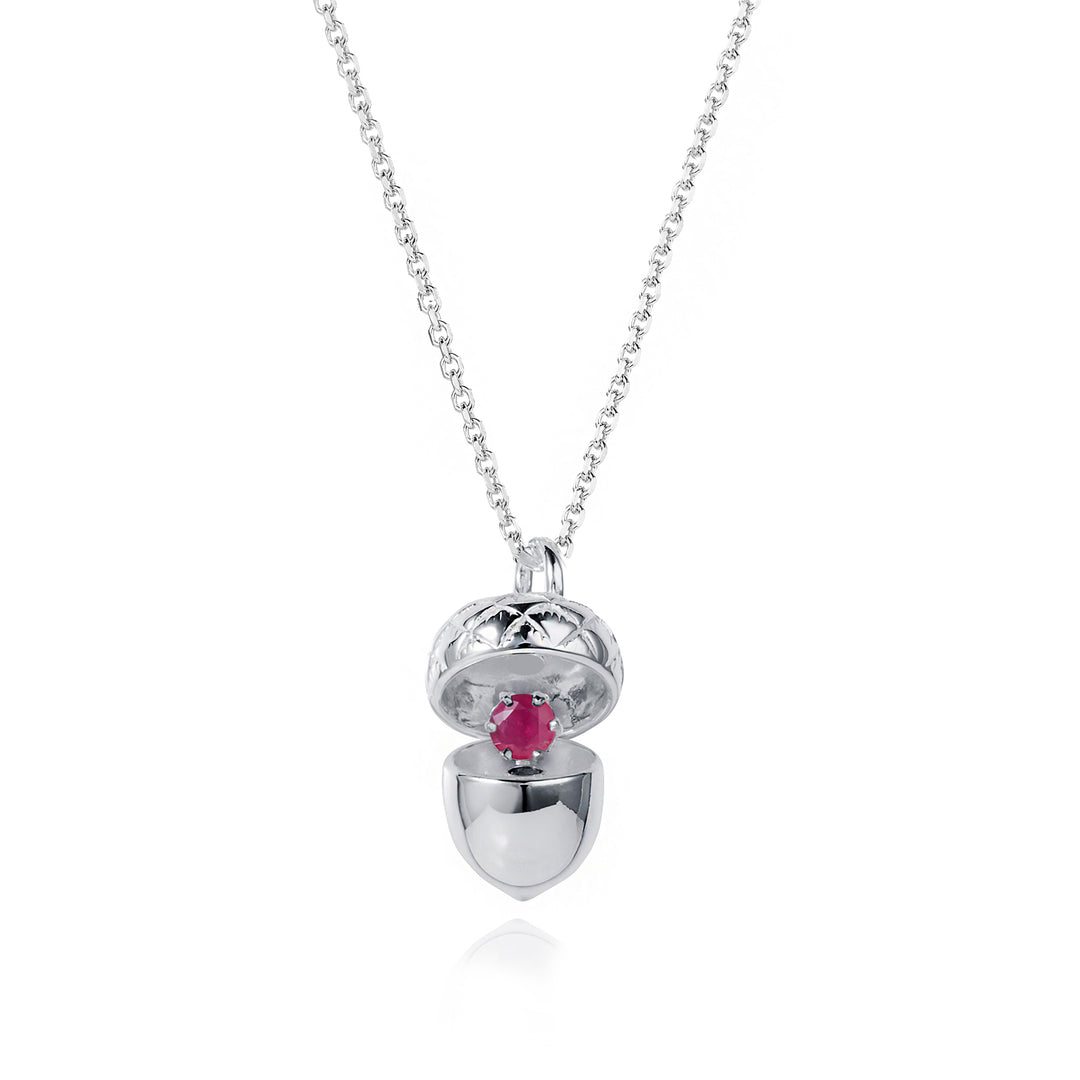 Silver acorn locket opened up to show a ruby july birthstone on a white background