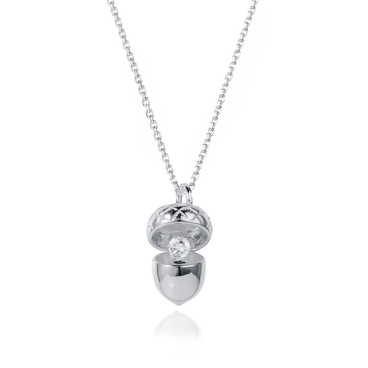 Silver acorn locket opened up to show a white topaz april birthstone on a white background