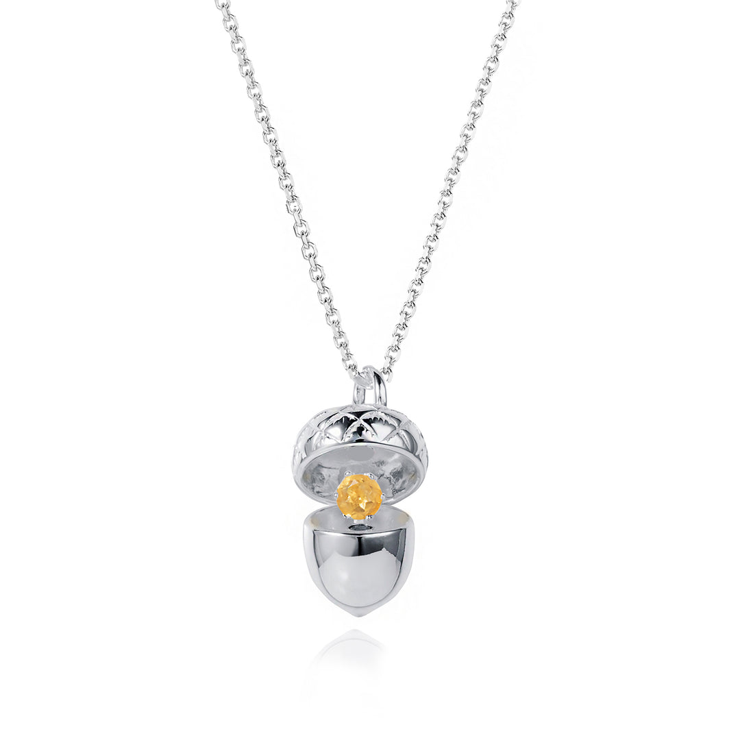 Silver acorn locket opened up to show a citrine november birthstone on a white background
