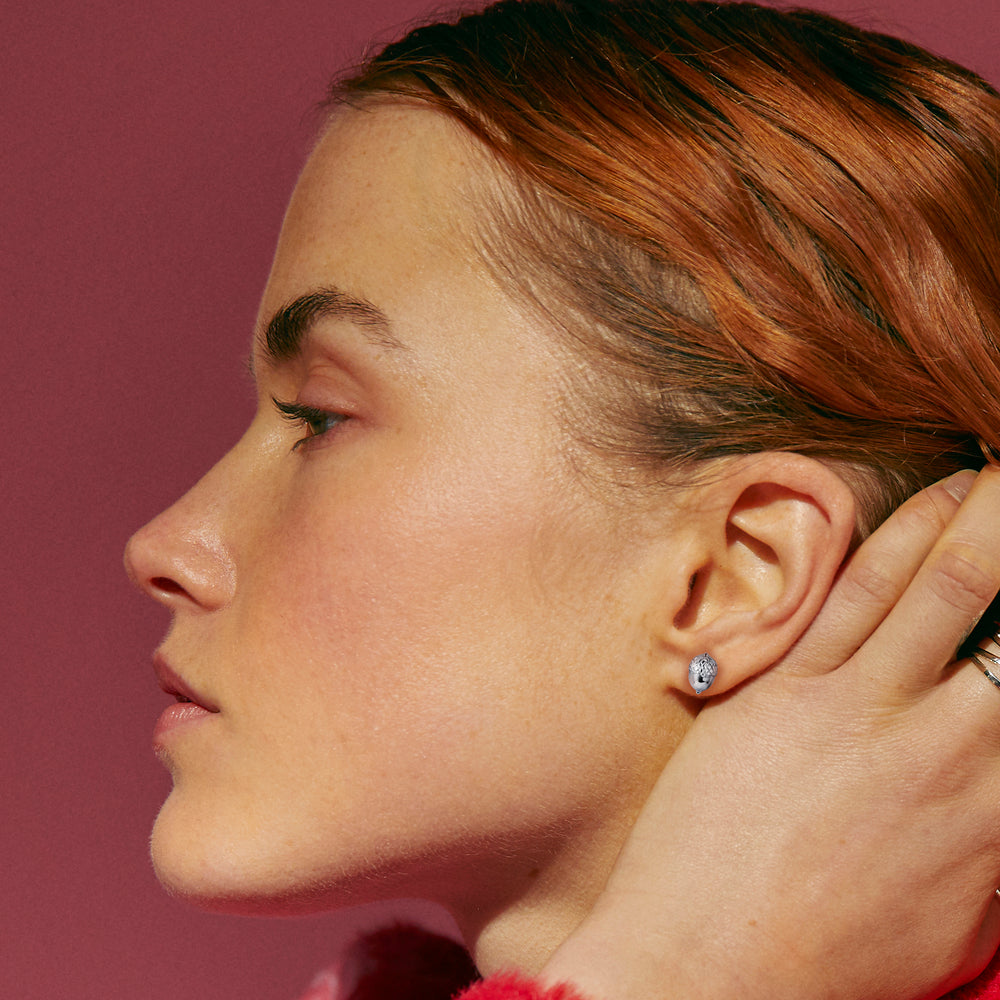 Close-up of a person wearing silver acorn earrings against a red background