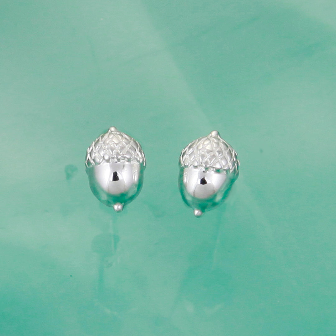 Pair of silver acorn-shaped earrings on a light green background