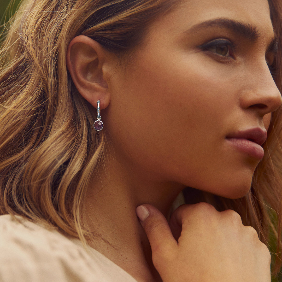 Model wearing silver hoop earrings with purple stone drops