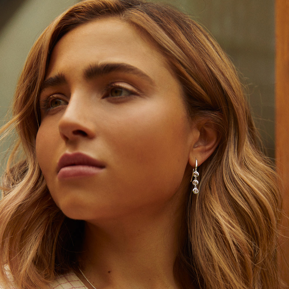 Close-up of woman wearing dainty silver drop earrings with amethyst gemstones in an outdoor environment