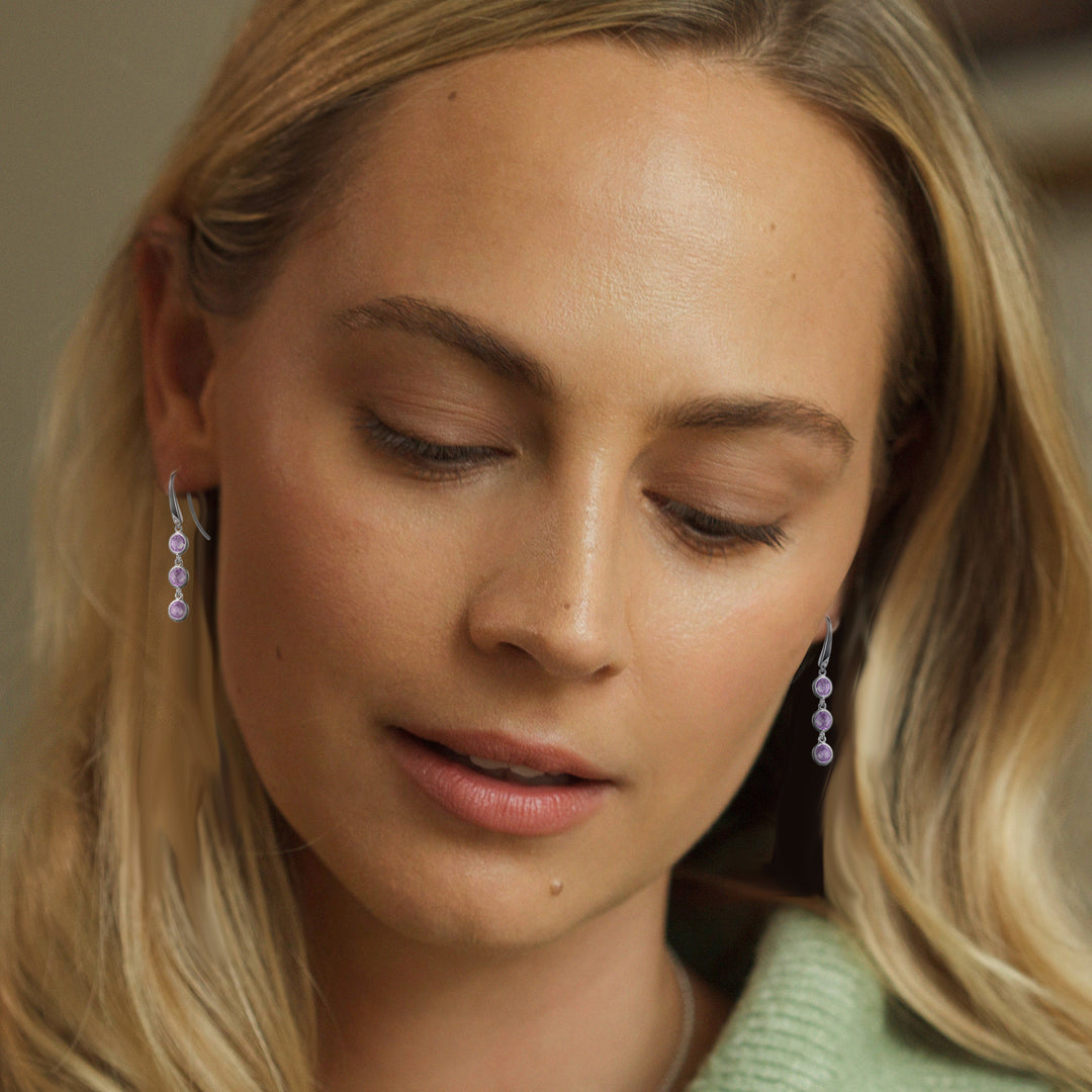 Close-up of a woman wearing silver drop earrings set with three amethyst gemstones