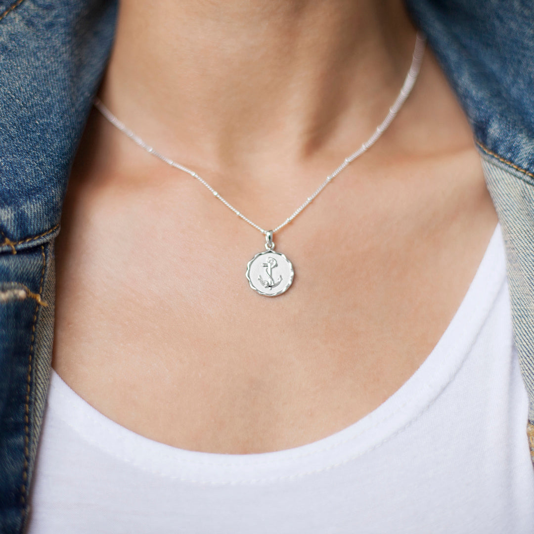 Close-up of model wearing a silver anchor pendant necklace and jeans jacket
