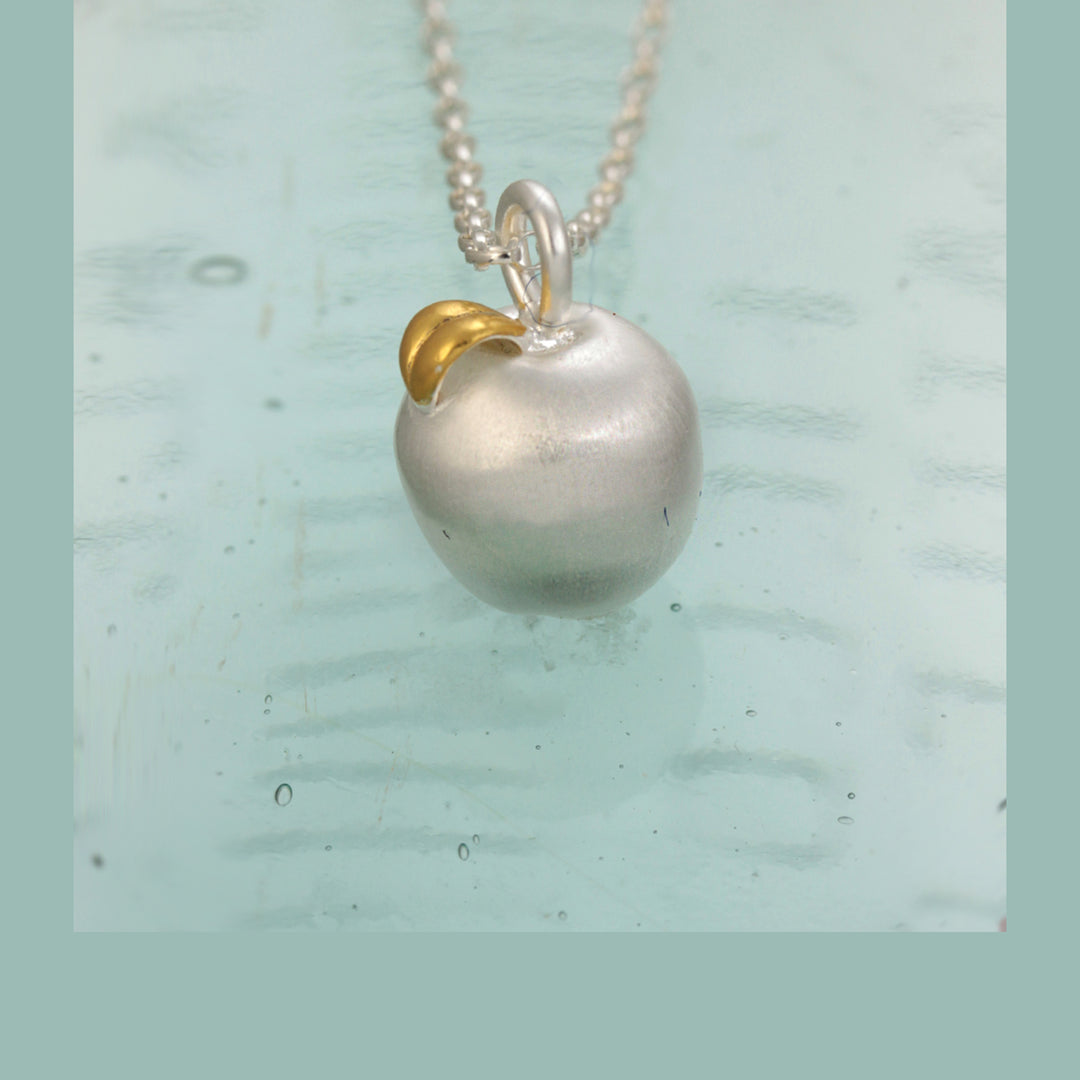 Silver apple necklace with a gold leaf on a light blue background