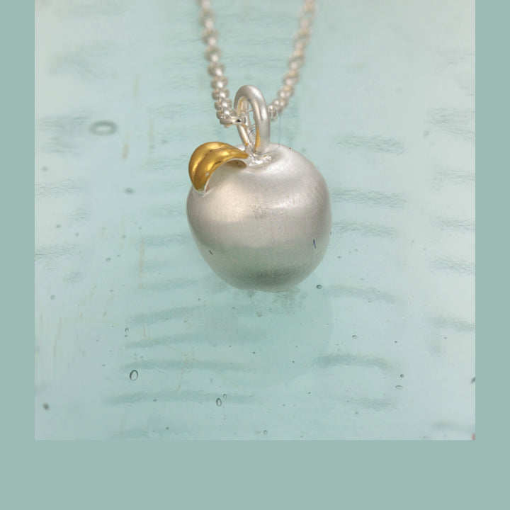 Silver apple necklace with a gold leaf on a light blue background
