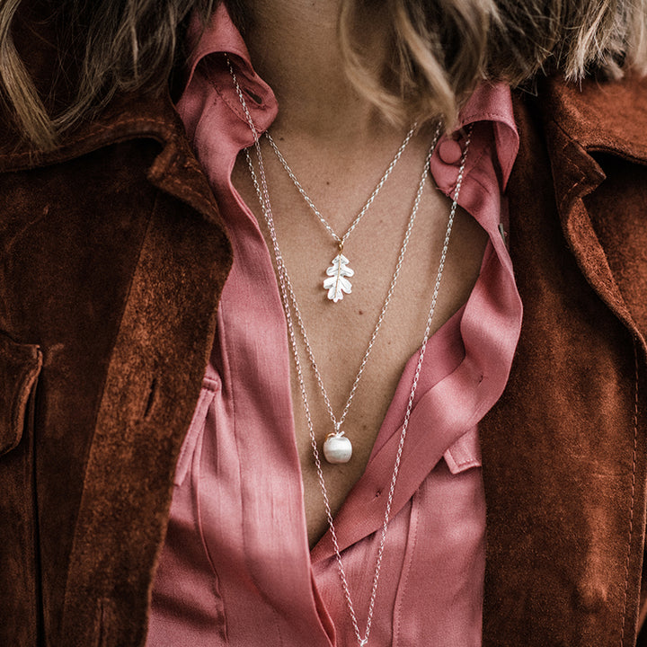 Person wearing layered necklaces, including a silver apple with a gold leaf 