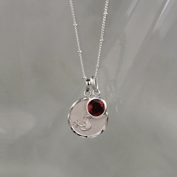 Silver aquarius zodiac pendant with a garnet january birthstone charm on gray background