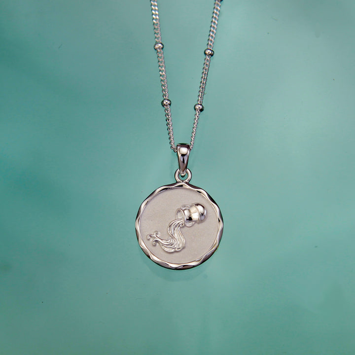 SIlver aquarius zodiac pendant and chain on an aqua background