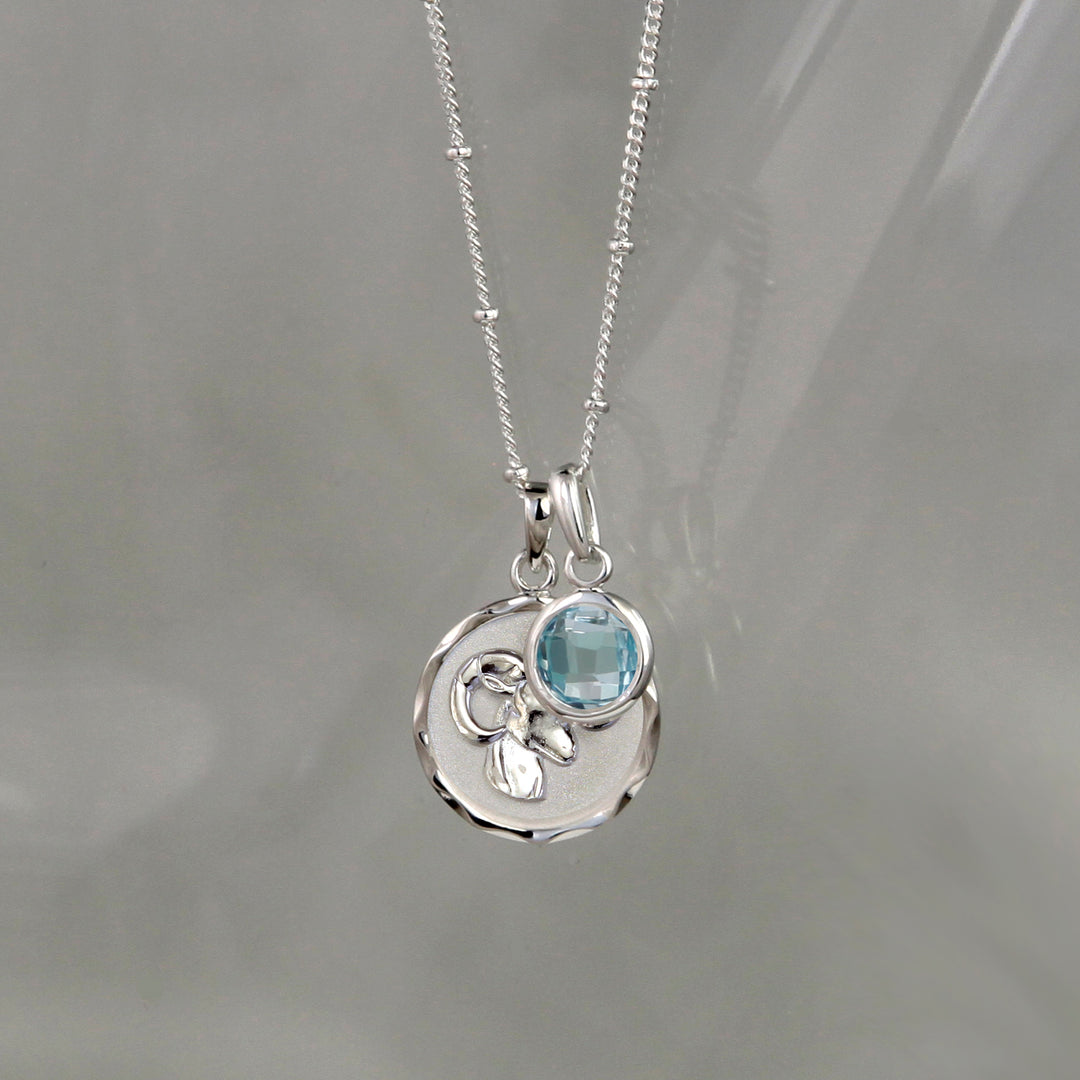 Silver Aries zodiac pendant and chain with blue topaz birthstone charm on gray background