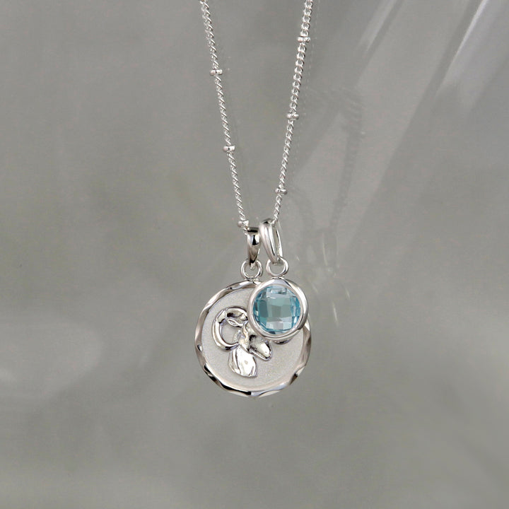Silver Aries zodiac pendant and chain with blue topaz birthstone charm on gray background
