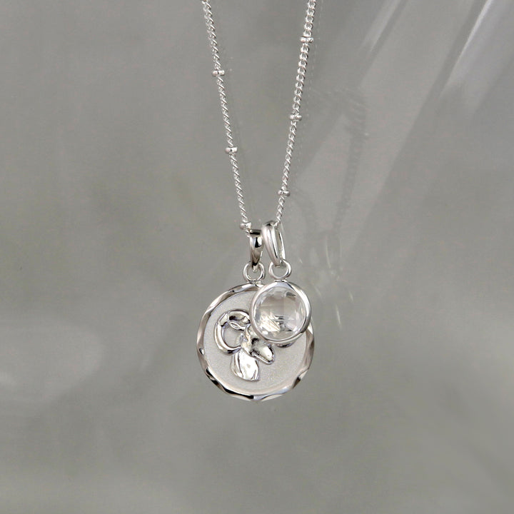 Silver Aries zodiac pendant and chain with silver topaz birthstone charm on gray background