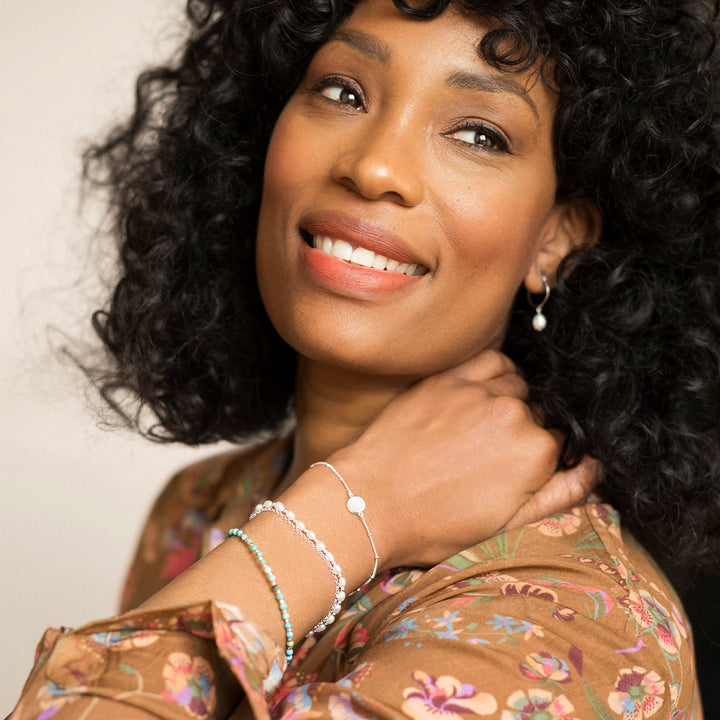 Model wearing three silver stacking bracelets with turquoise, moonstone and pearls.
