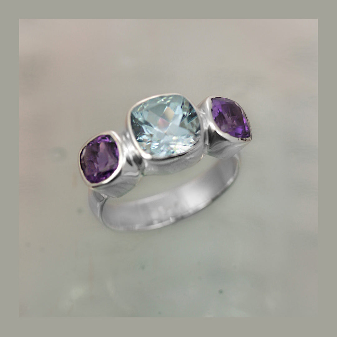 Brilliant blue topaz and amethyst cushion-cut gemstone ring in silver against a gray background