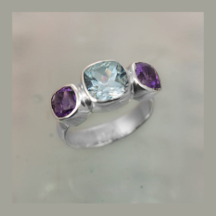Brilliant blue topaz and amethyst cushion-cut gemstone ring in silver against a gray background