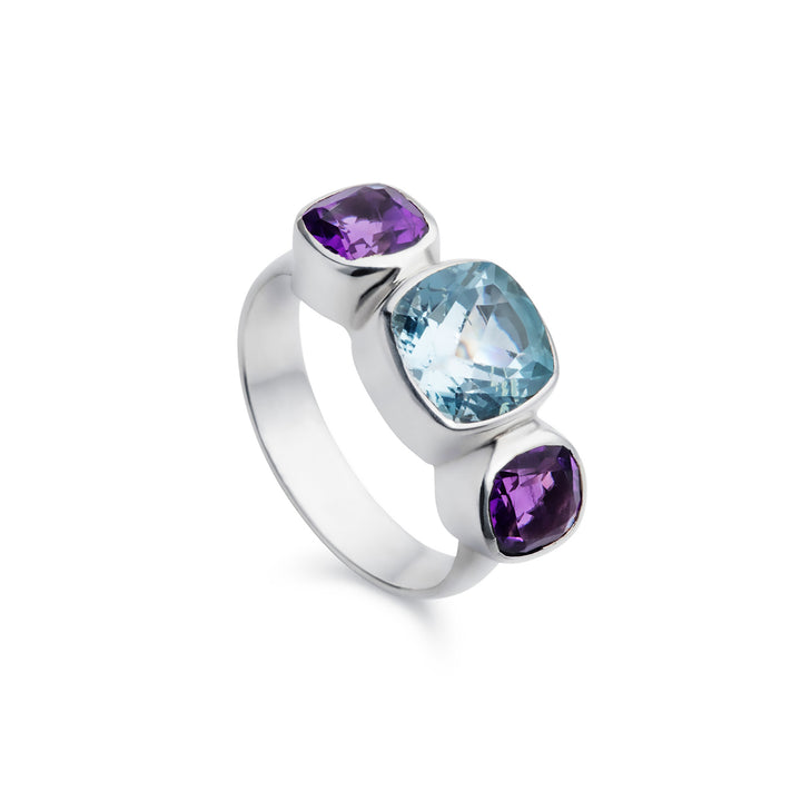 Silver three stone ring with blue topaz and amethysts on a white background