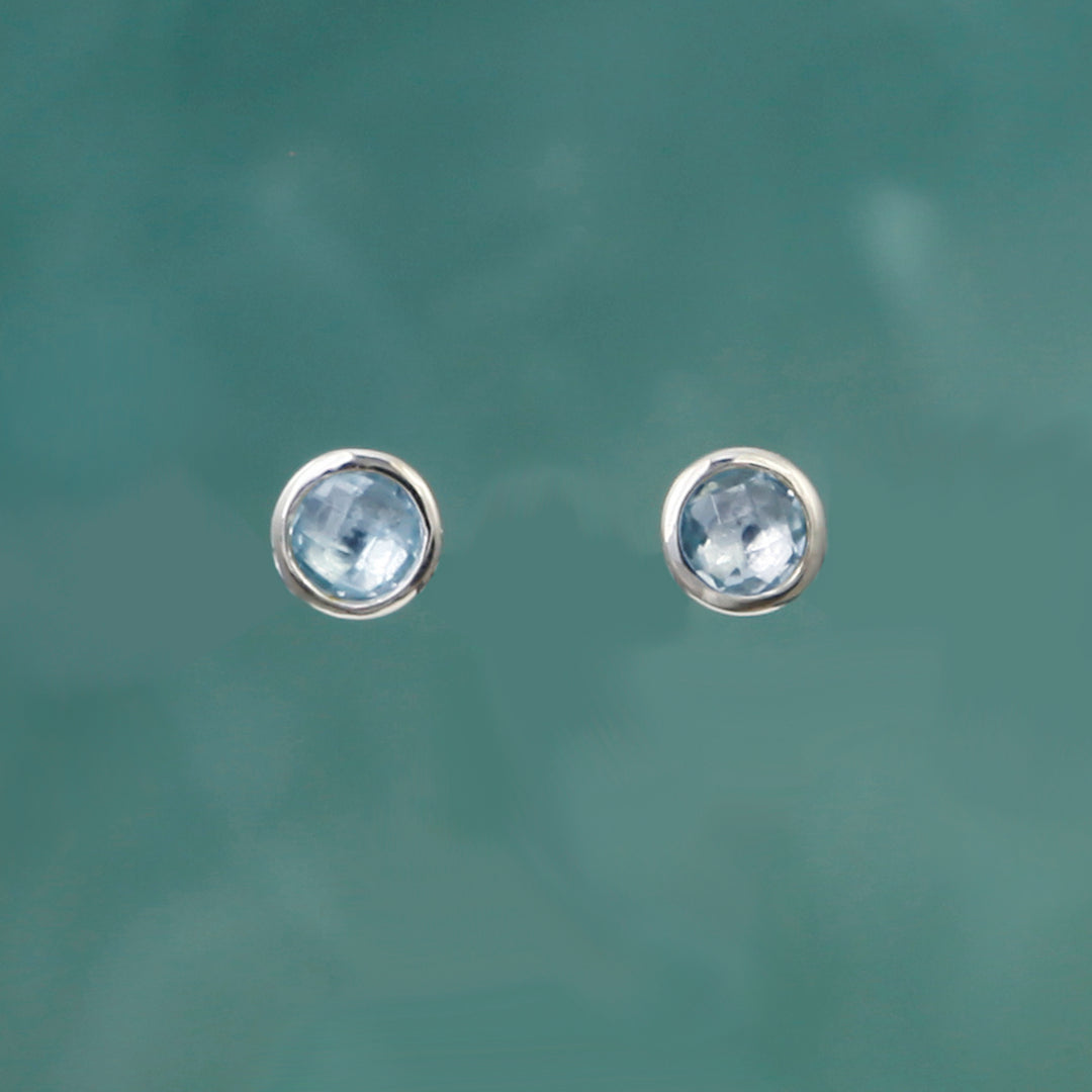 Round silver stud earrings with blue topaz on a teal background