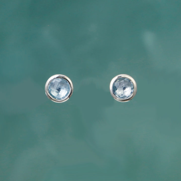 Round silver stud earrings with blue topaz on a teal background