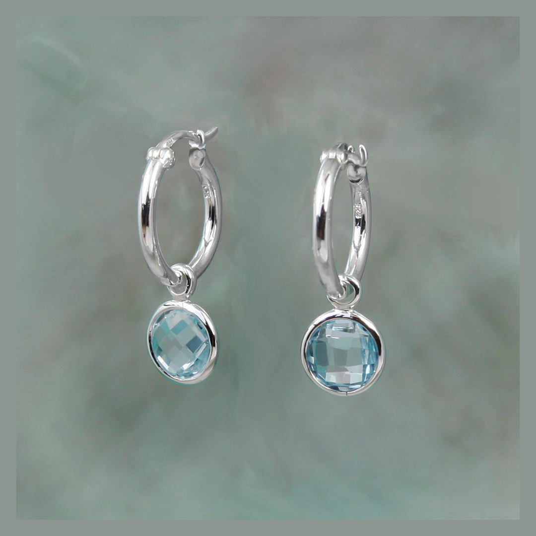 Silver hoop earrings with blue stone drops on a gray background