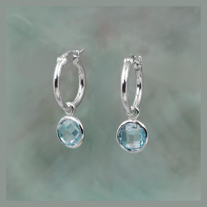 Silver hoop earrings with blue stone drops on a gray background