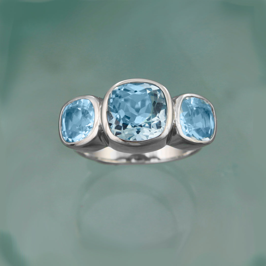 Front  view of a three cushion-cut blue topaz ring on aqua background