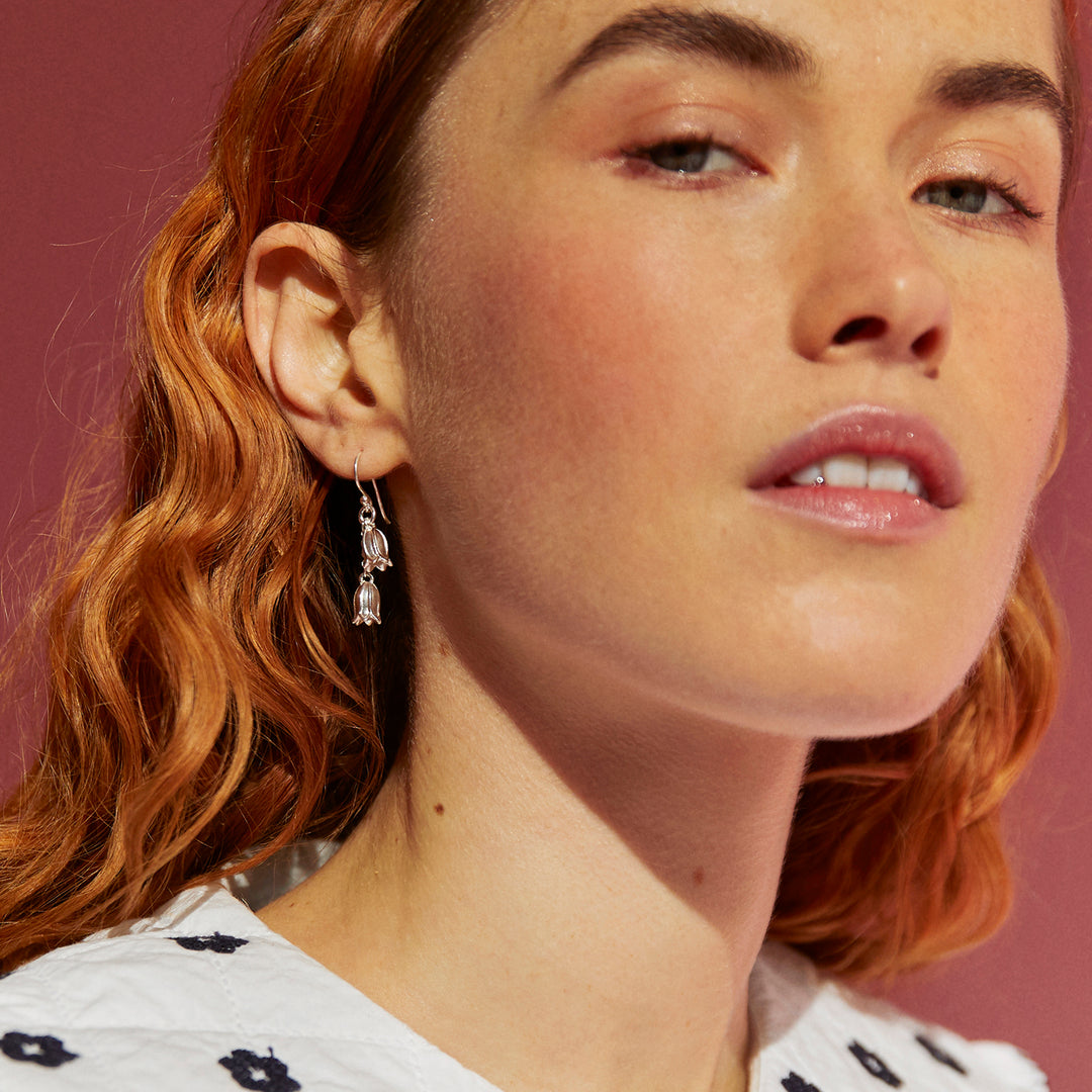 Close-up of a woman with red hair wearing silver flower earrings against a pink background
