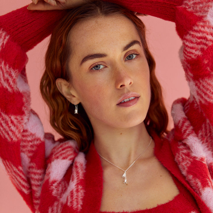 Model wearing silver bluebell shaped silver necklace and matching earrings with red and pink sweater