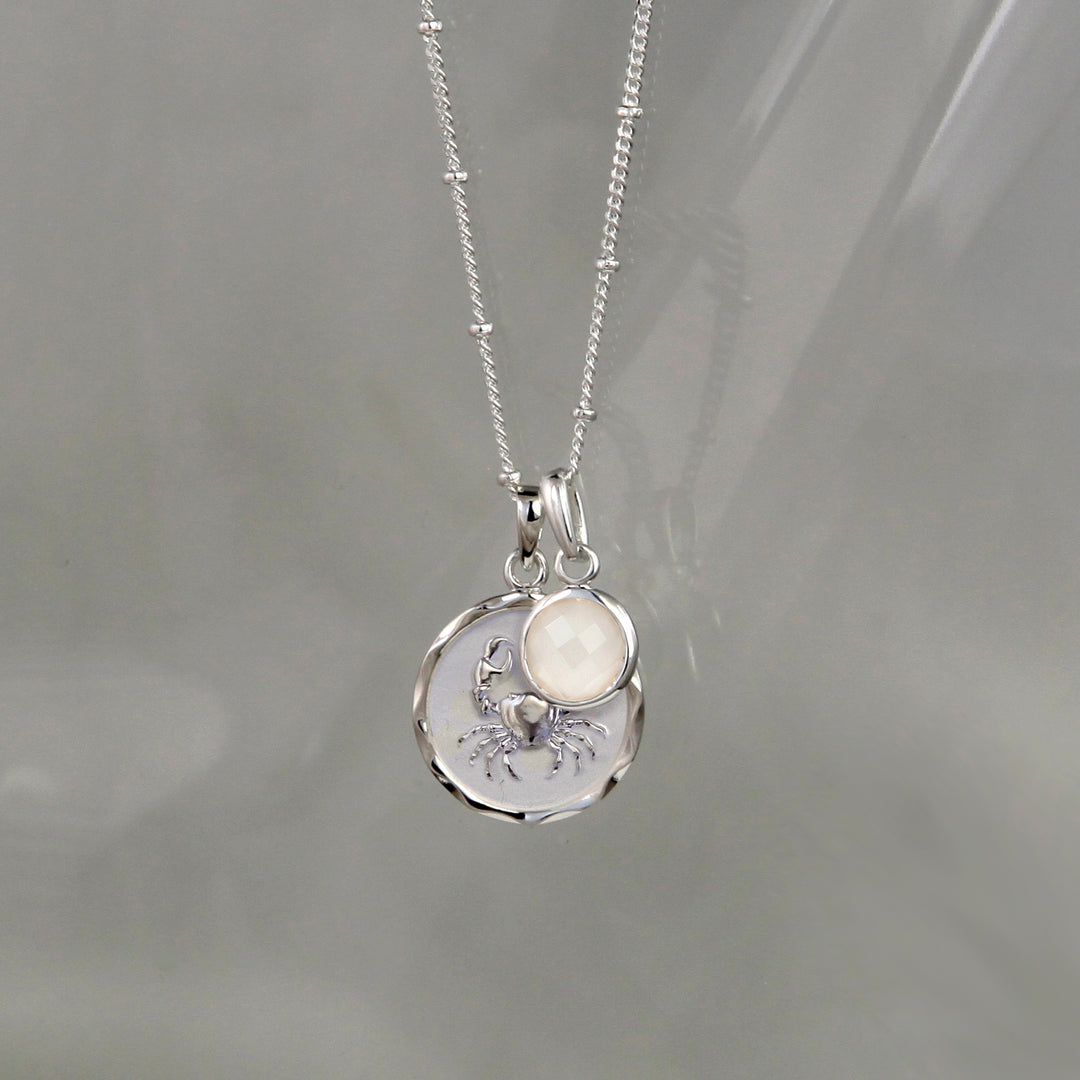 SIlver cancer zodiac pendant and moonstone June birthstone charm on a gray background