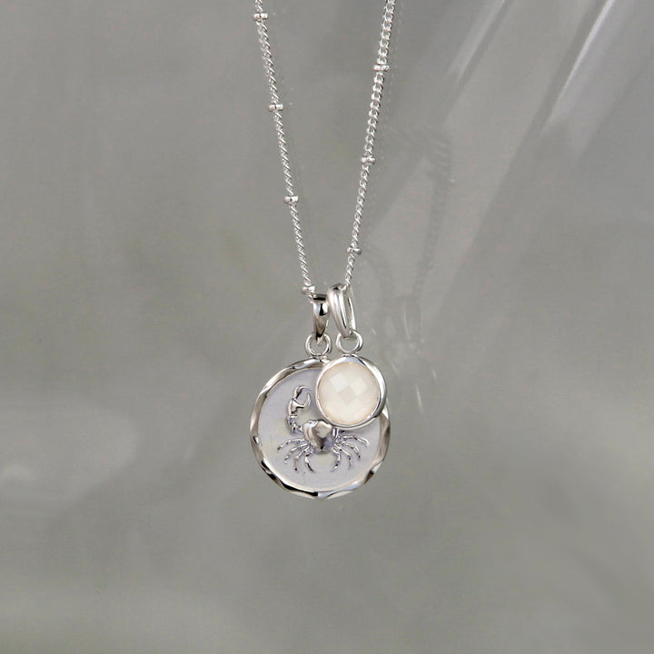 SIlver cancer zodiac pendant and moonstone June birthstone charm on a gray background