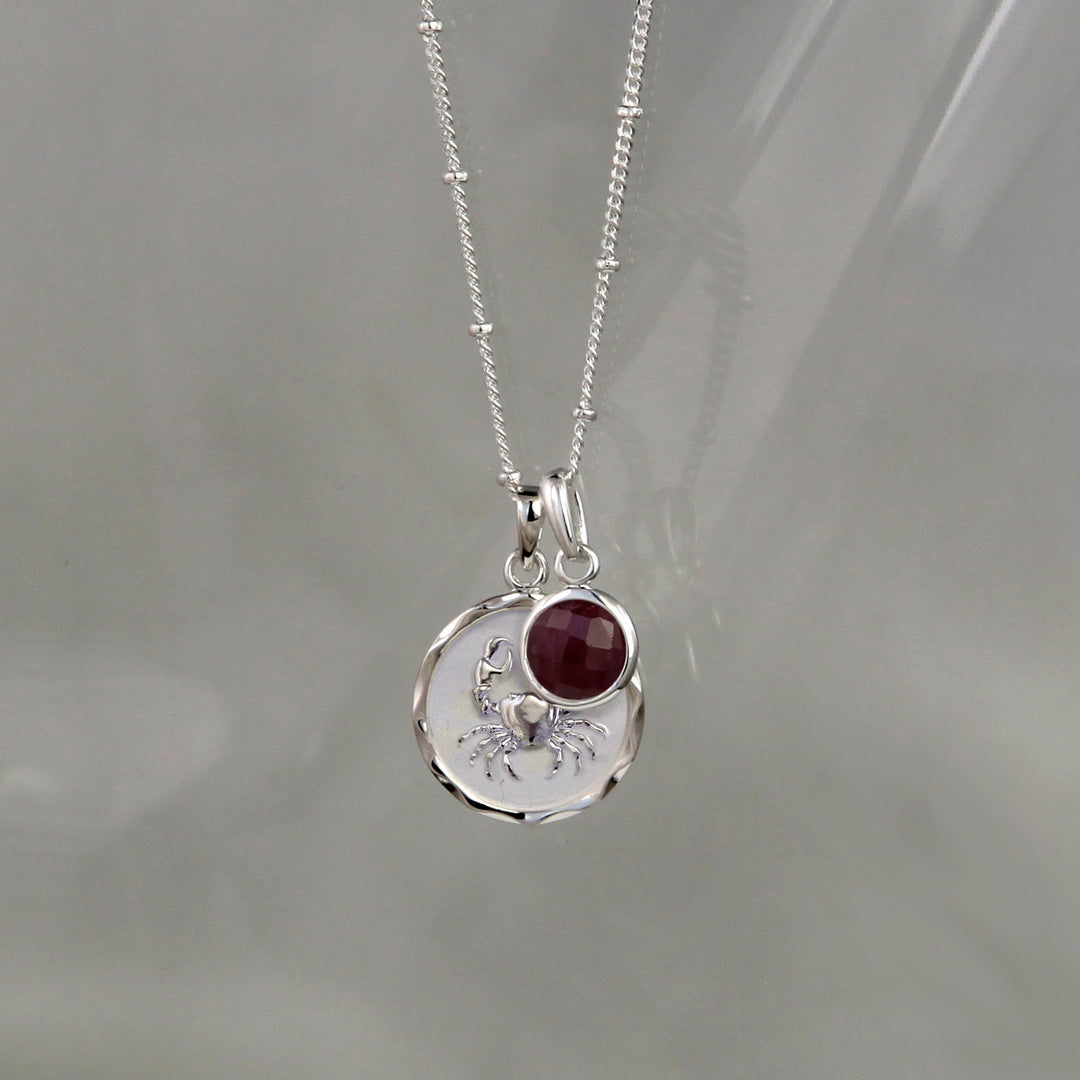 SIlver cancer zodiac pendant and ruby july birthstone charm on a gray background