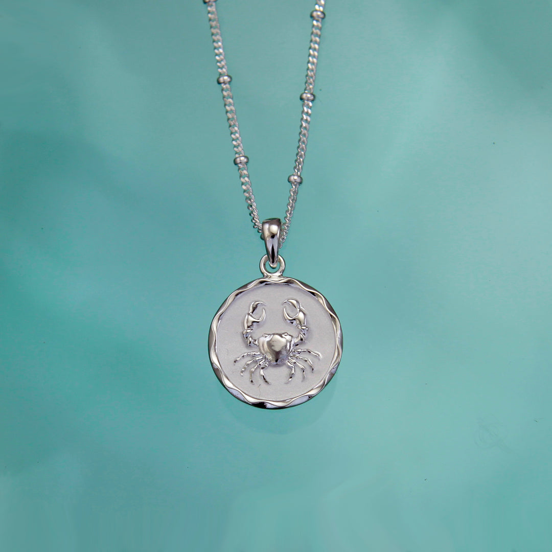 Silver cancer crab pendant against a teal background