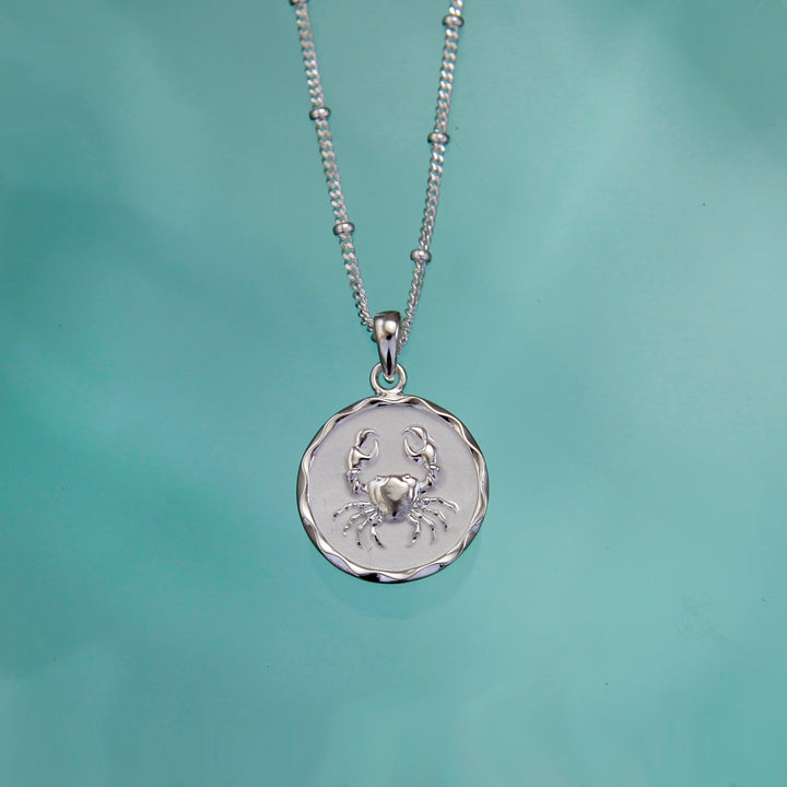 Silver cancer crab pendant against a teal background