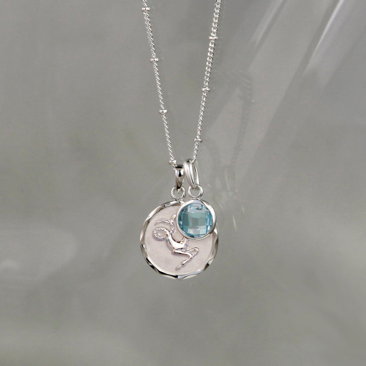 Silver capricorn zodiac necklace with a blue topaz december birthstone charm