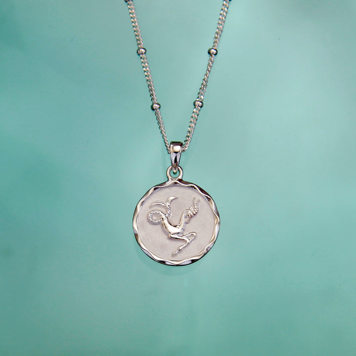 silver capricorn star sign necklace against an aqua background